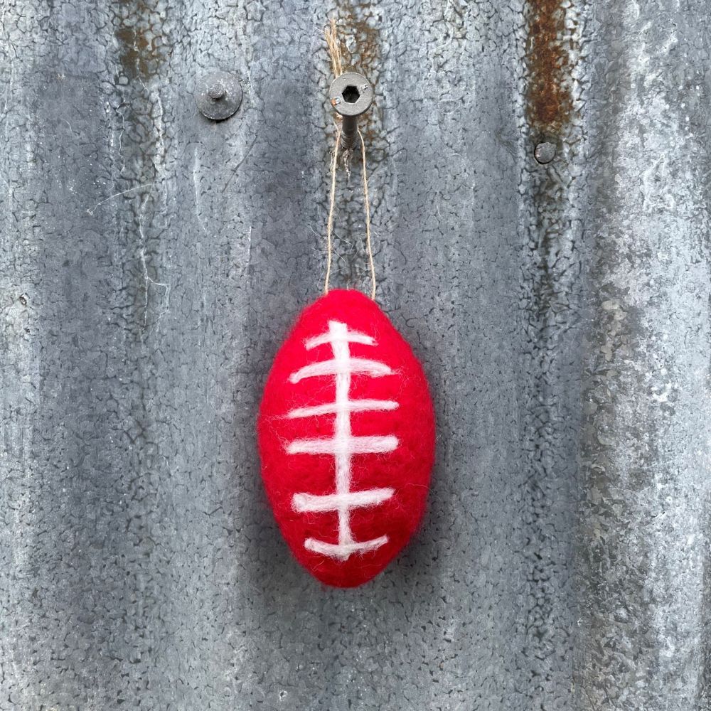 Red felt football ornament with white lines hanging on a textured metal surface