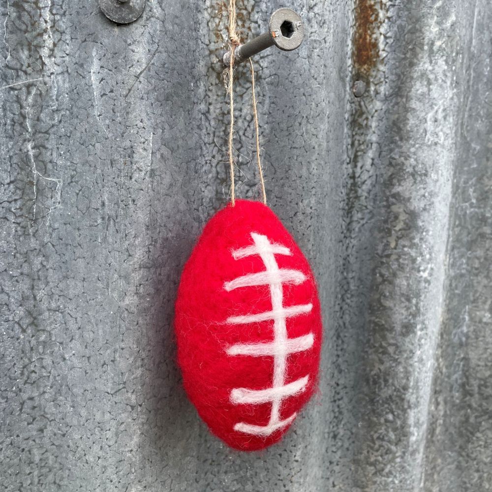 Red felt football ornament hanging on a textured metal surface