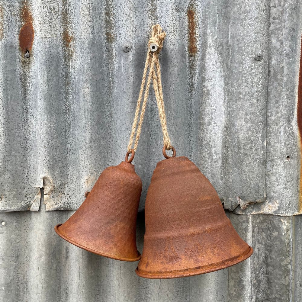 Two rusted bells hanging on a corrugated metal wall.