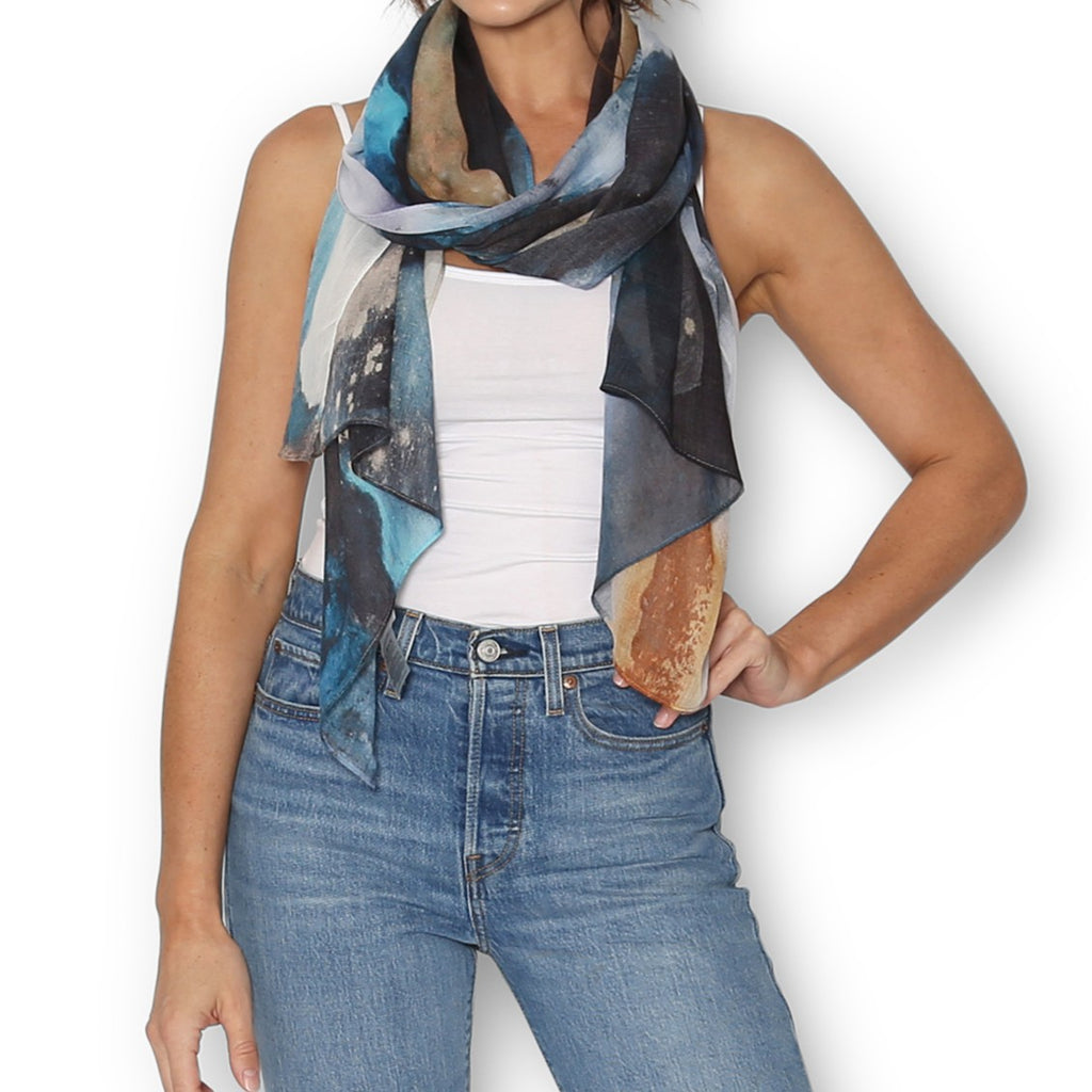 Woman wearing a The Artist Label Transcend colorful scarf and blue jeans on a white background