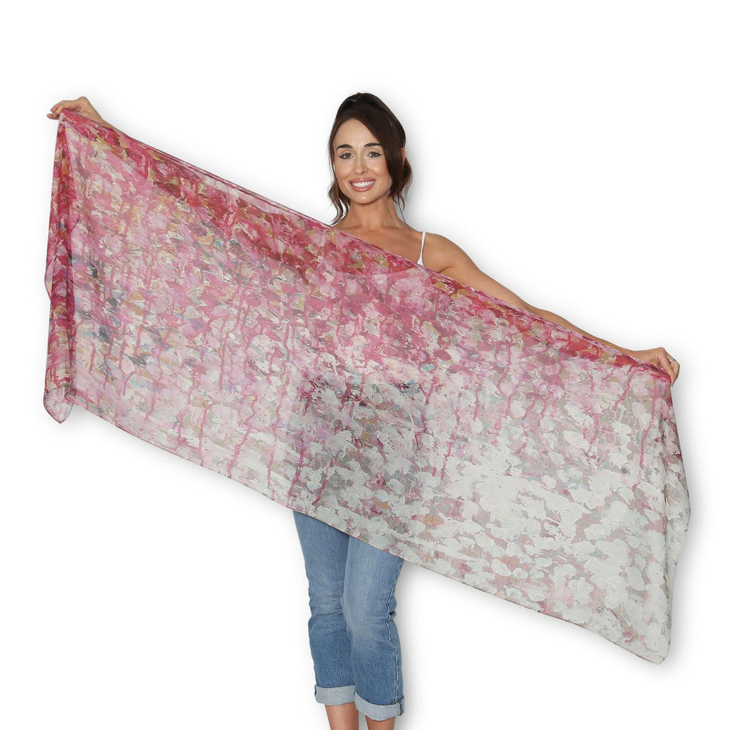 Woman holding up The Artist Label Pink Primrose patterned scarf, in shades of pink with hints of gold and blue.