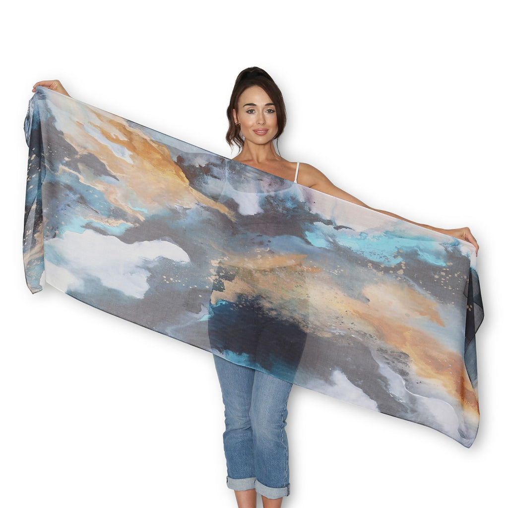 Woman holding a The Artist Label Transcend scarf with a scenic design on a white background