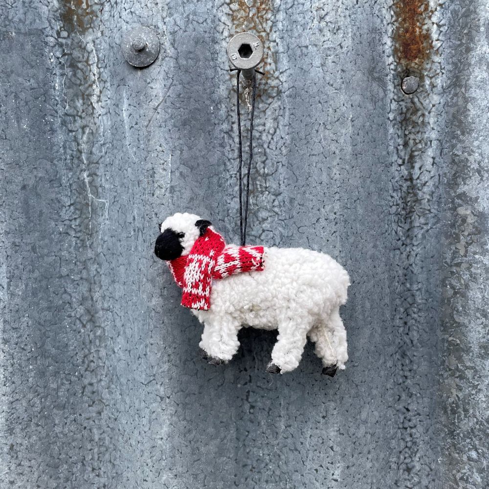 White sheep ornament with a red scarf hanging on a textured metal surface