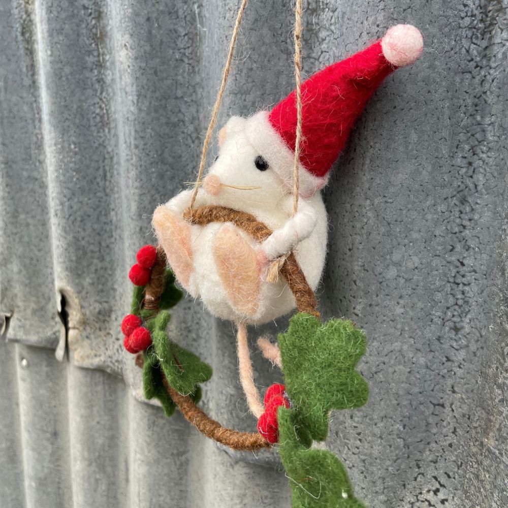 Felted mouse ornament with Santa hat on a wire against a textured metal background