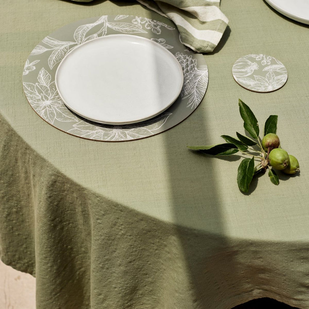 Table setting with white plates, mineral green tablecloth, and decorative elements on a round table.