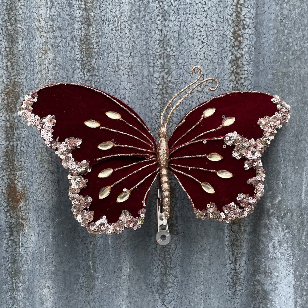Decorative butterfly with burgandy wings and gold accents against a textured metal background.