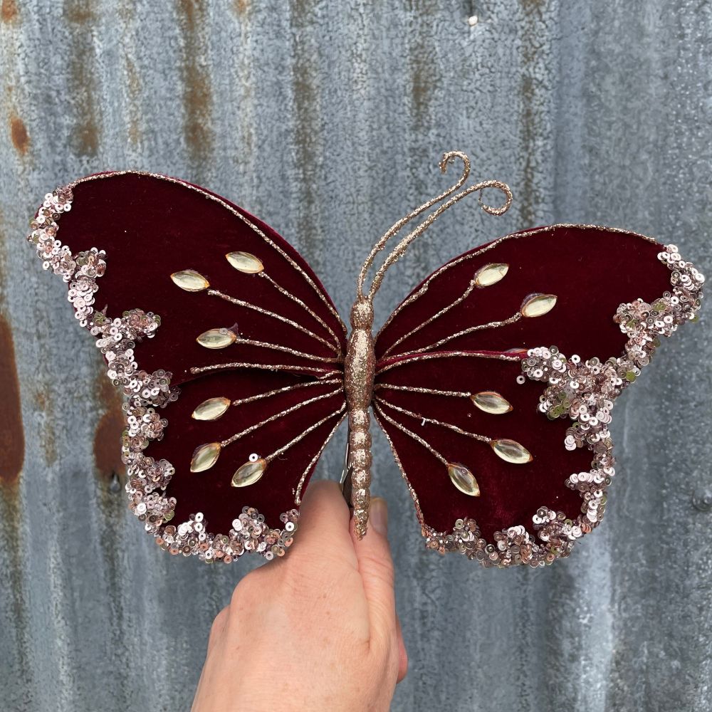 Decorative butterfly with maroon wings and gold accents held against a textured metal background.