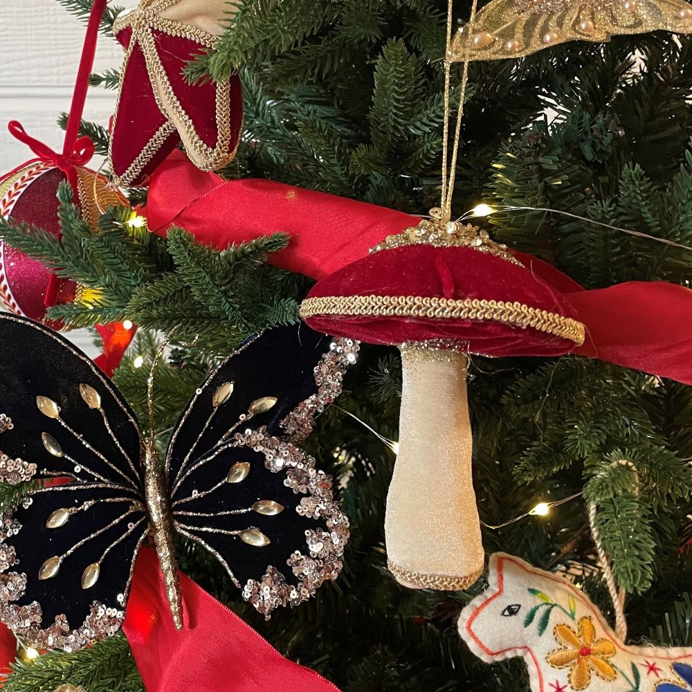 Decorative mushroom ornament on a Christmas tree with red ribbon and other ornaments.
