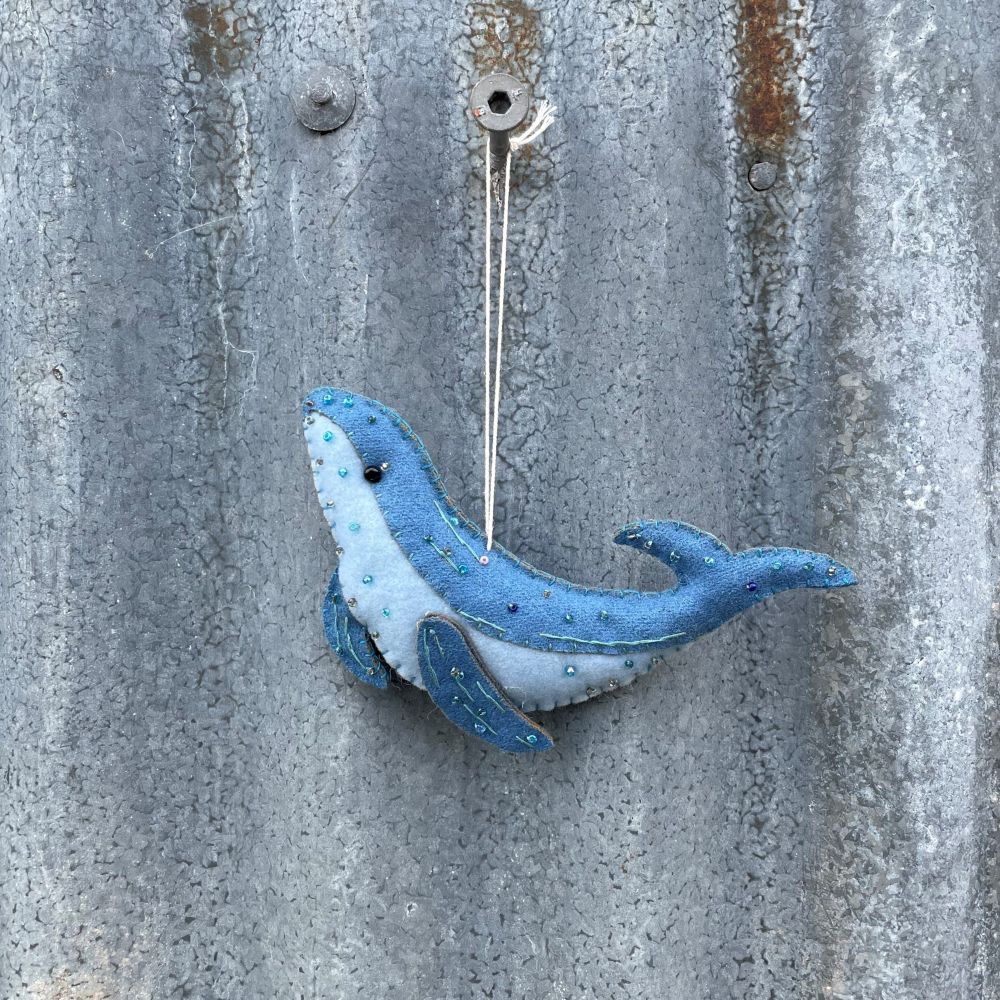 Blue felt whale ornament hanging on a textured metal surface