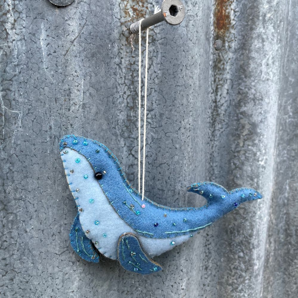 Blue felt whale ornament hanging on a textured metal surface - closer view