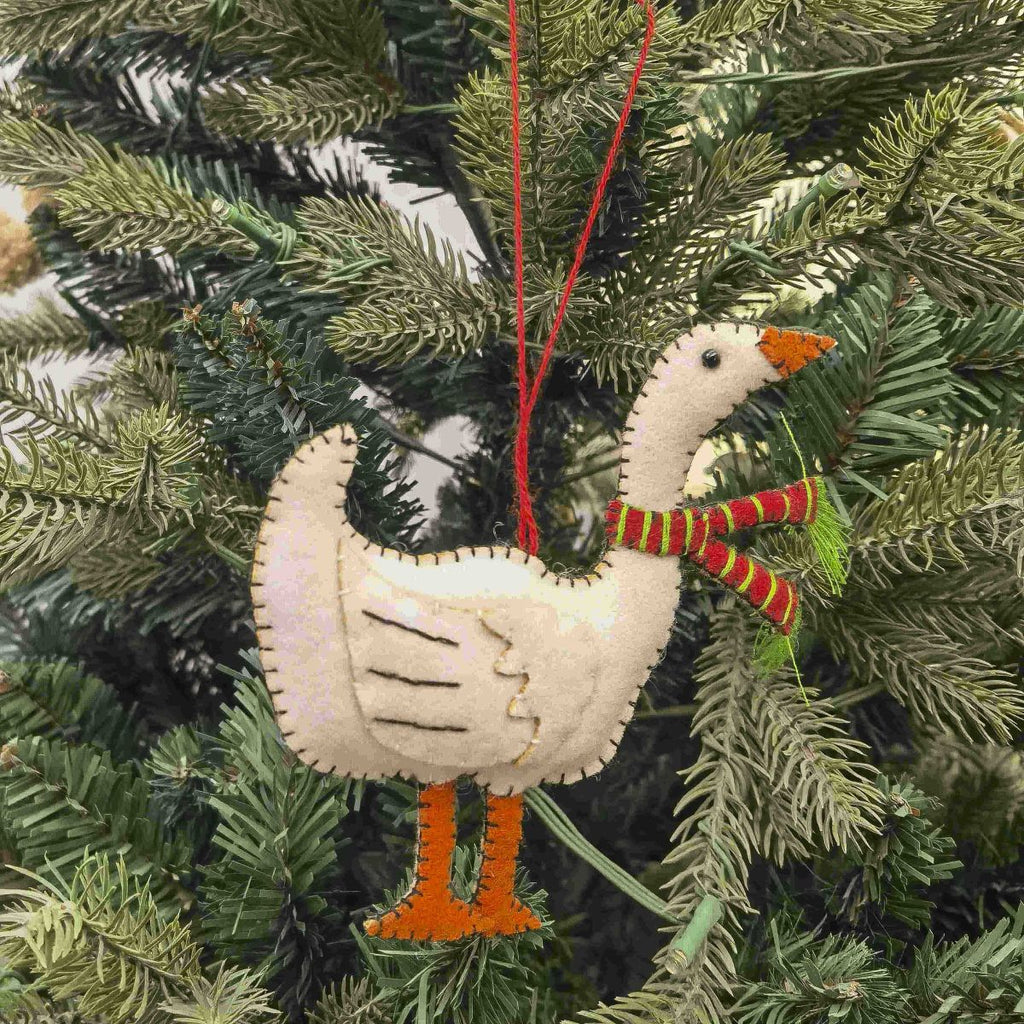 Decorative goose ornament with a red and green striped scarf hanging on a Christmas tree.