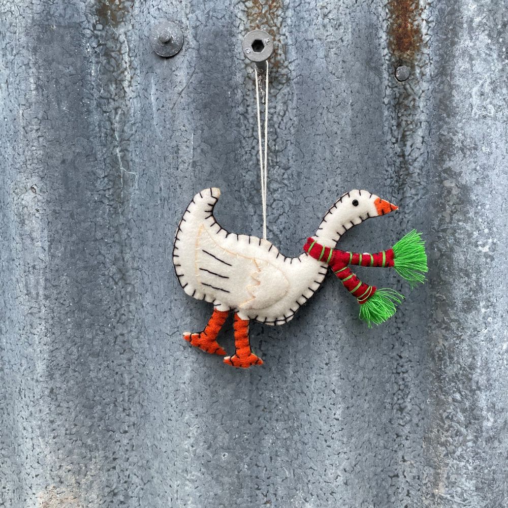 Decorative felt goose ornament with a striped scarf and green tail feathers hanging on a metal surface.