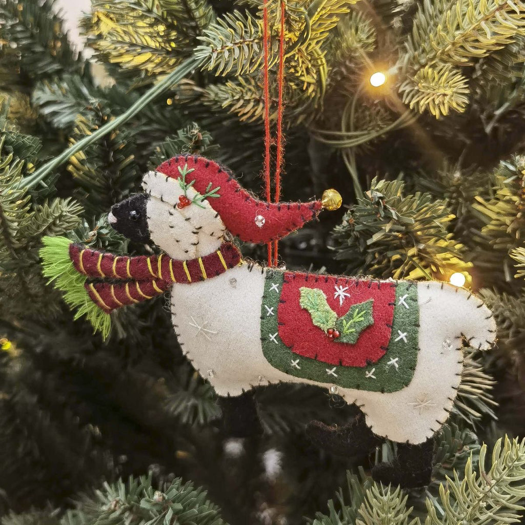Felt sheep ornament with red hat and scarf hanging on a Christmas tree.