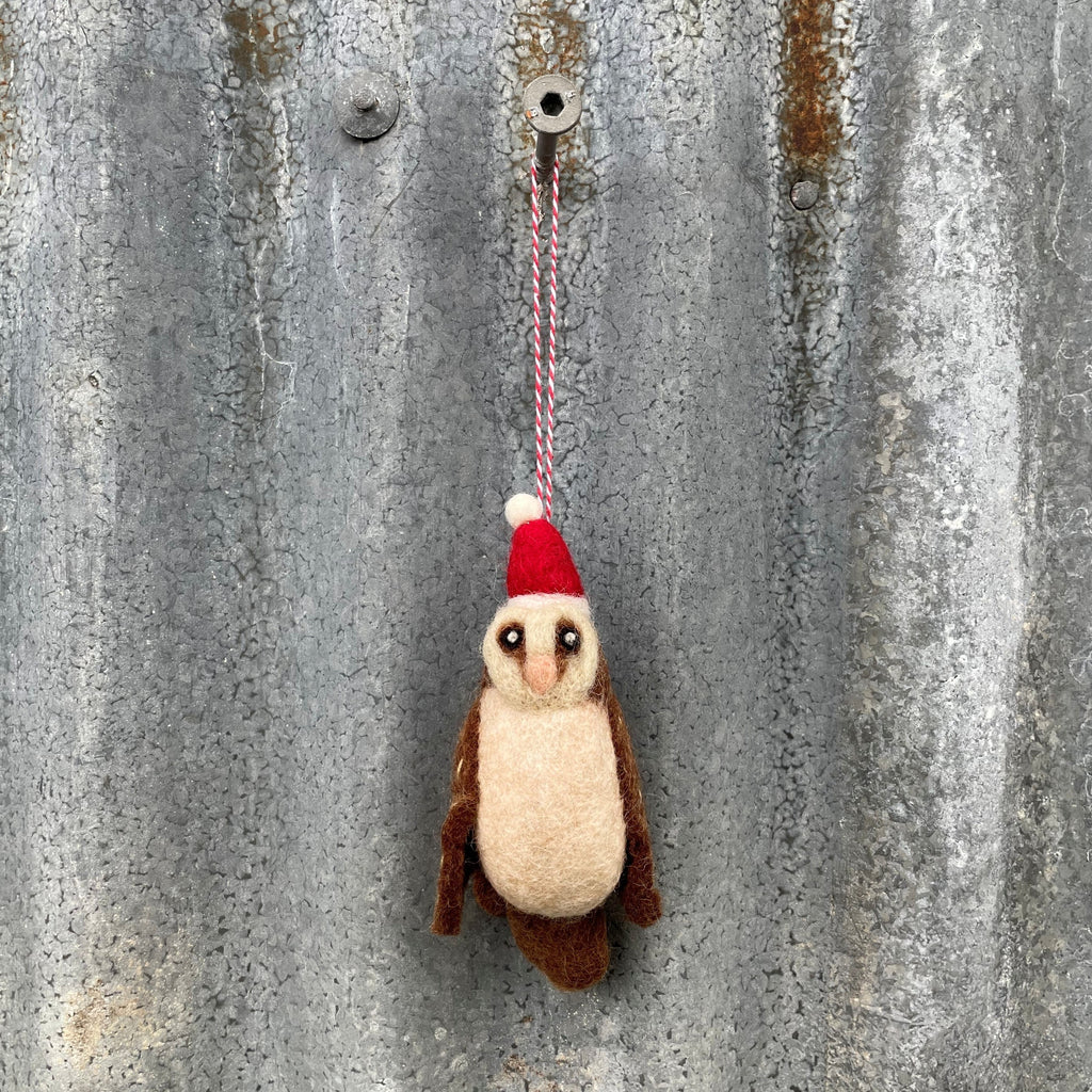 Felted owl ornament with a red hat hanging on a textured metal surface