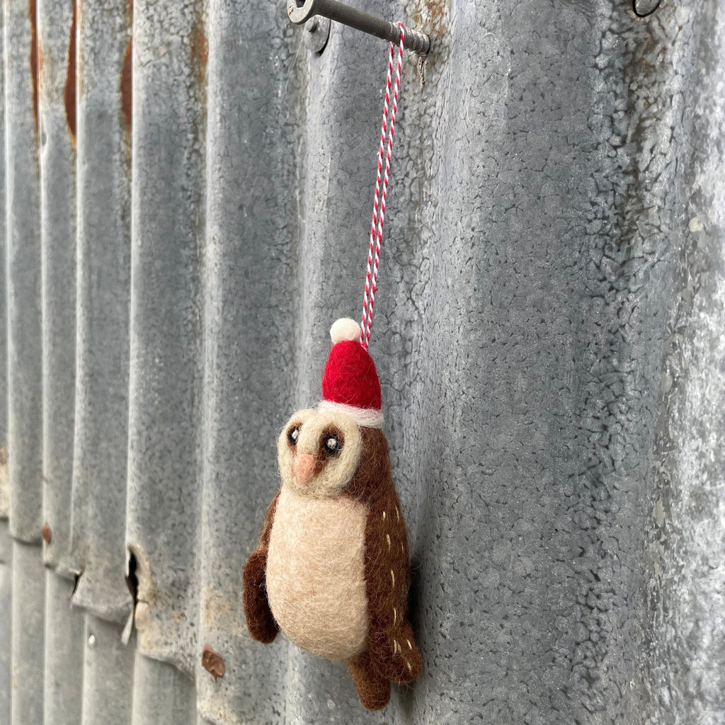 Felted owl ornament wearing a Santa hat hanging on a metal surface.