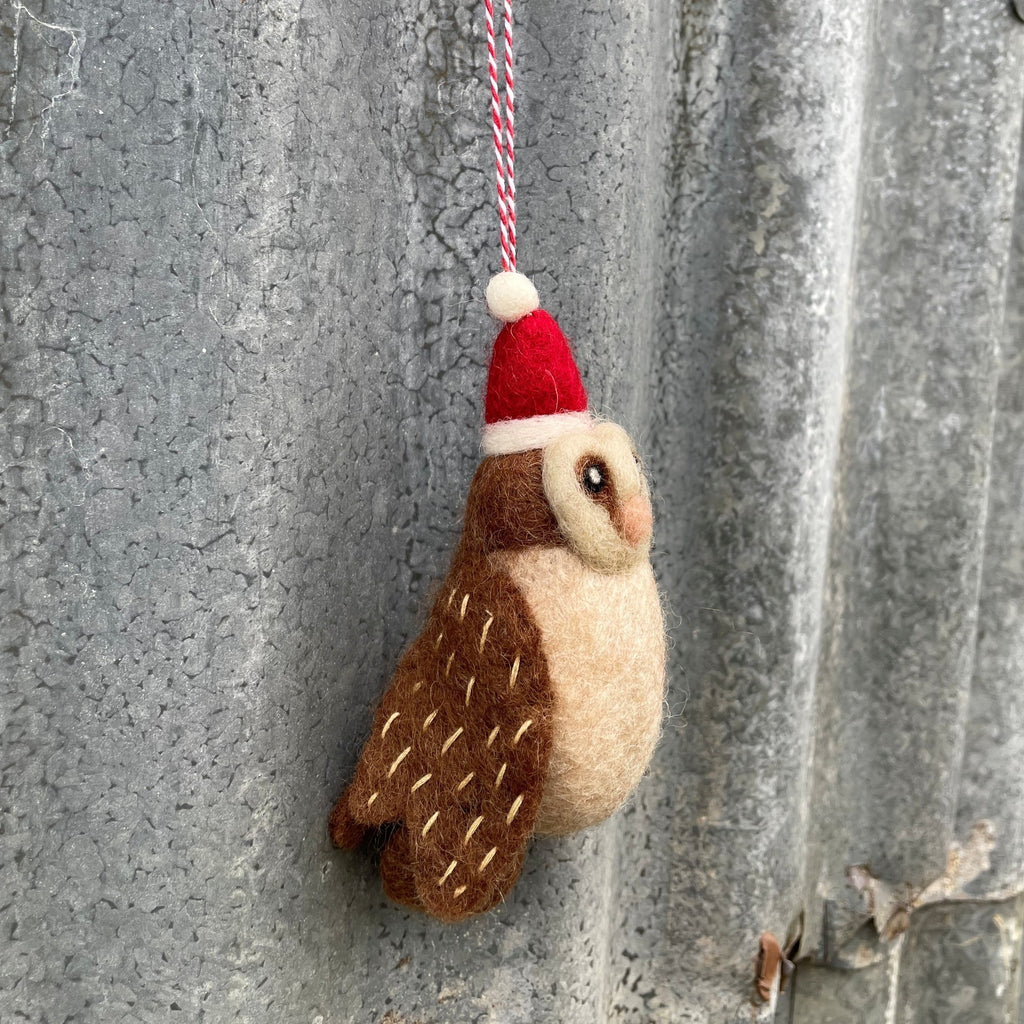 Felt owl ornament with a Santa hat hanging on a textured wall.