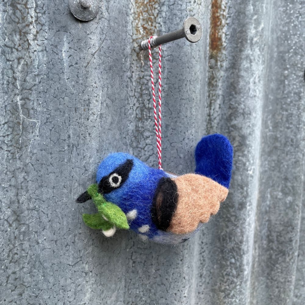 Felted Australian blue wren bird ornament hanging on a textured metal surface