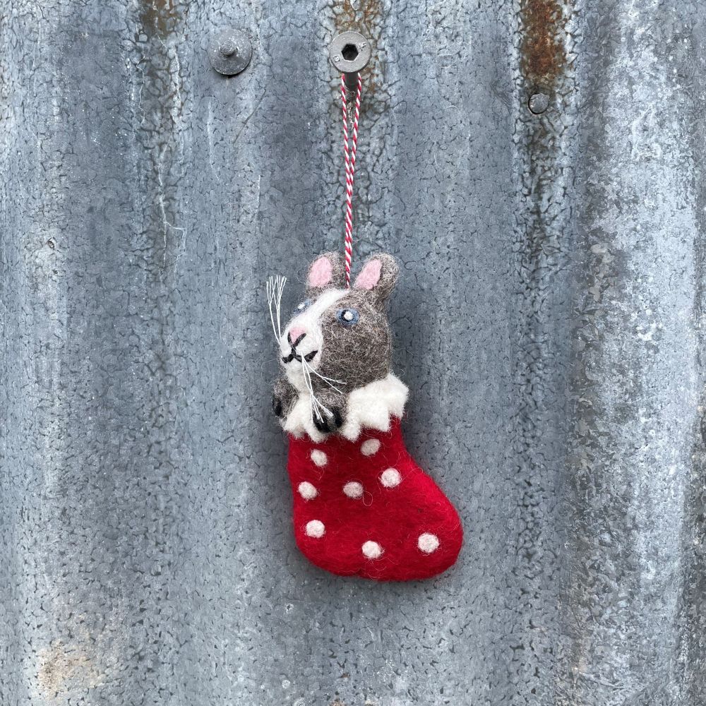 Felt cat in a red stocking with white polka dots hanging on a textured metal surface.