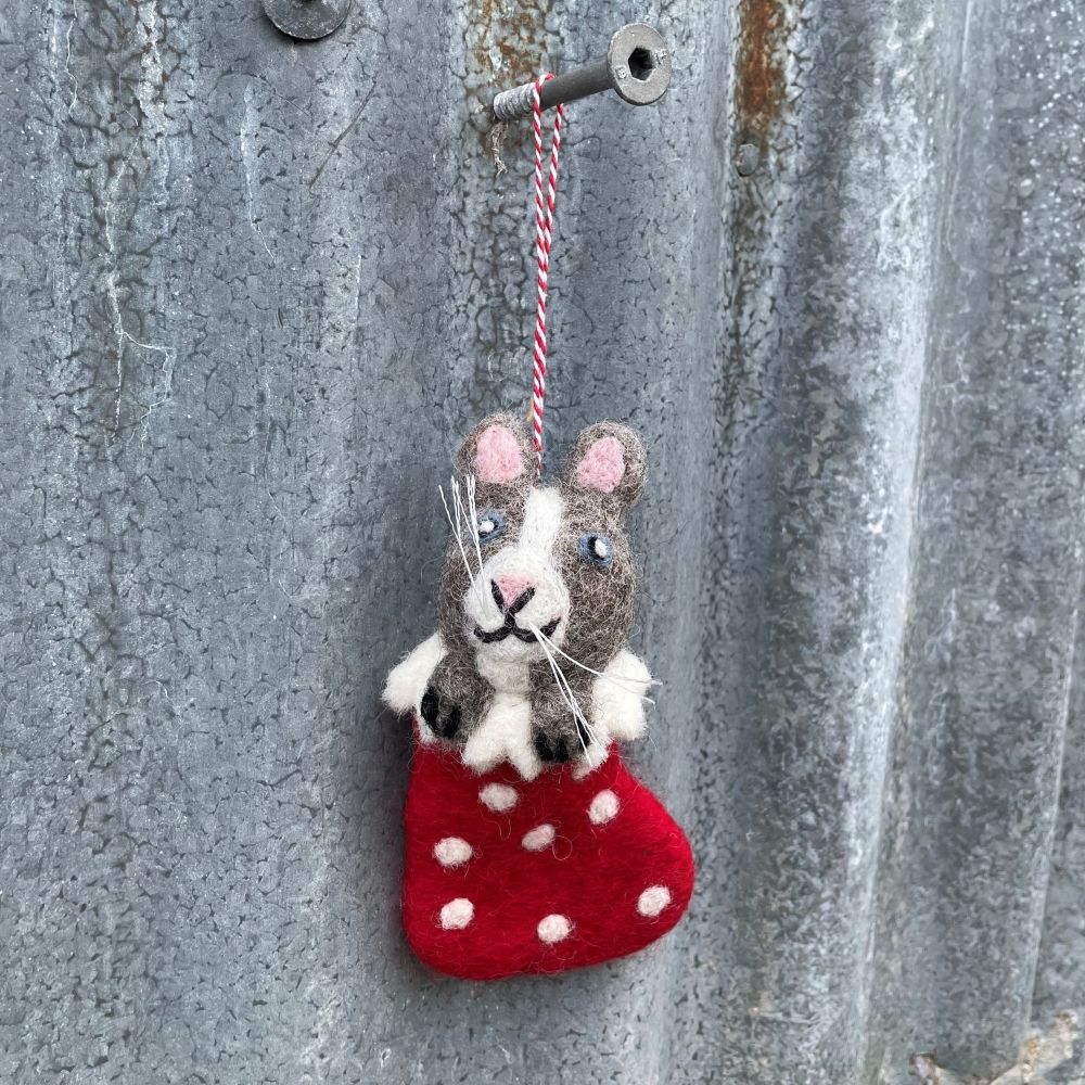 Felt cat in a red stocking with white polka dots hanging on a textured metal surface.