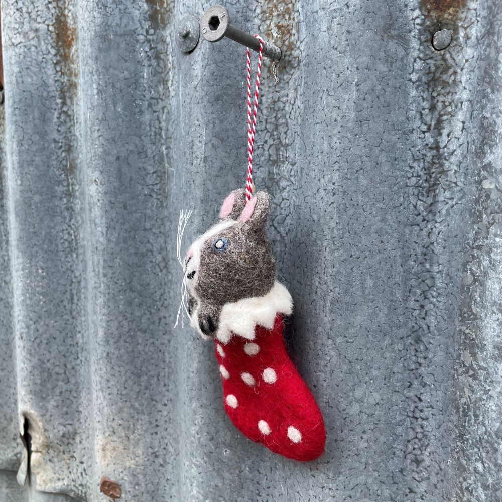 Felt cat in a red stocking with white polka dots hanging on a textured metal surface.