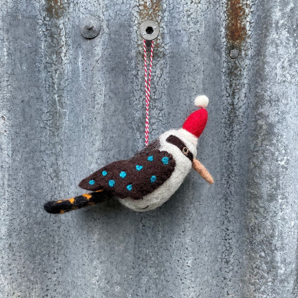 Felted Australian kookaburra ornament with a red hat hanging on a textured metal surface