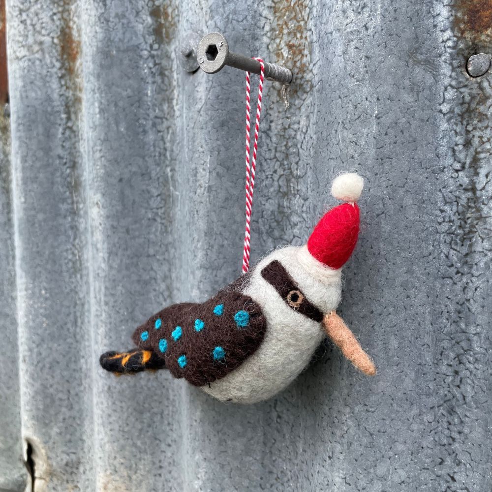 Felted Australian kookaburra ornament with a red hat hanging on a textured metal surface