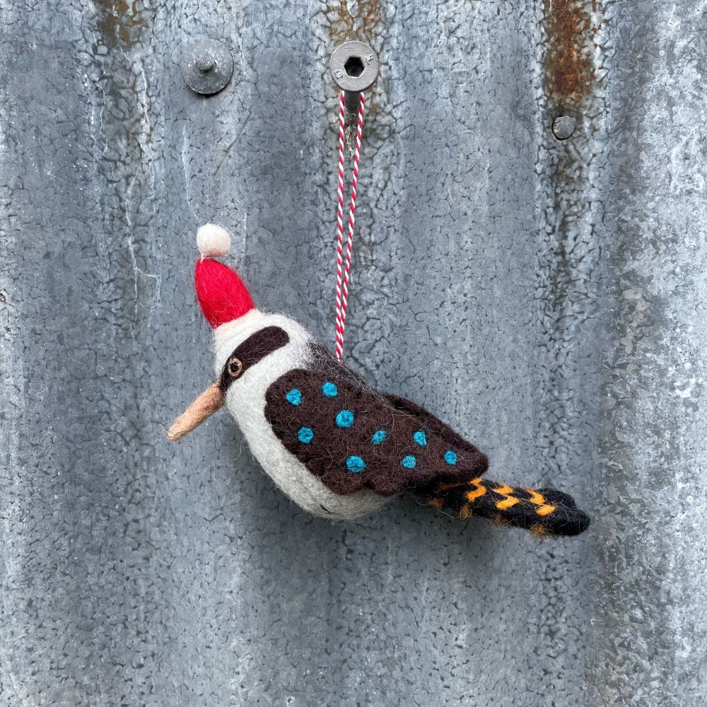 Felted Australian kookaburra ornament with a red hat hanging on a textured metal surface