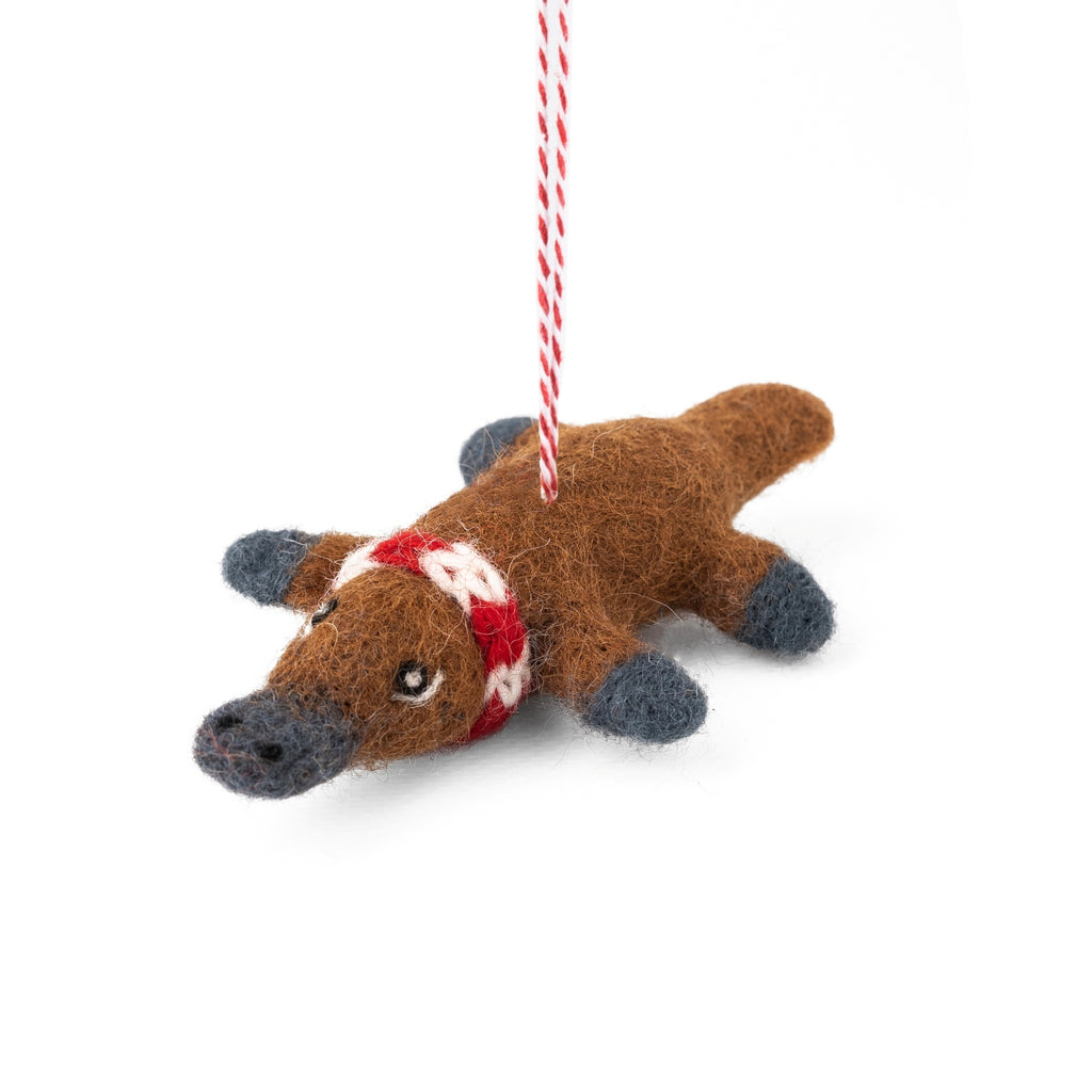 Felted platypus ornament with a red scarf hanging on a white background