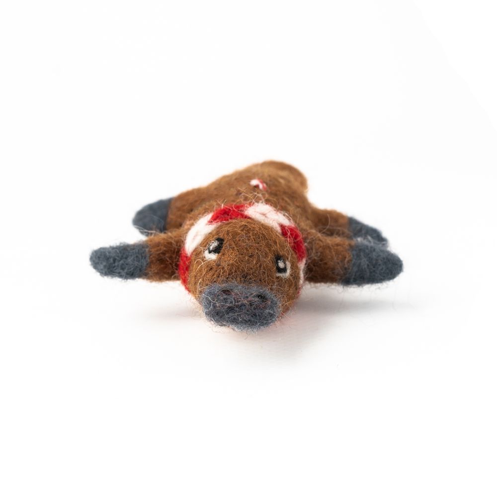 Felted platypus hanging Christmas decoration in brown with a red scarf on a white background