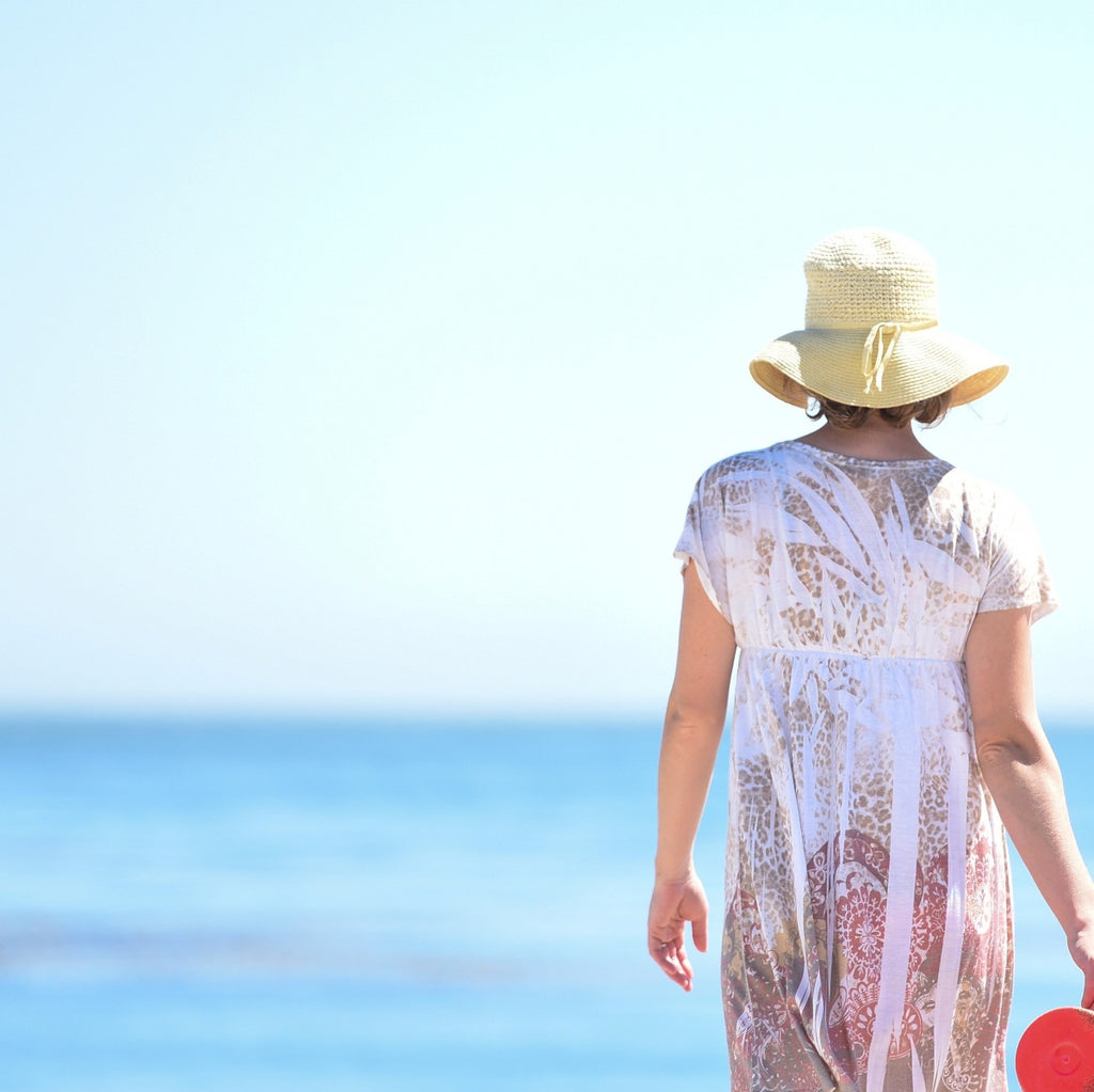 Person wearing a white lace dress and straw hat against a clear blue water.
