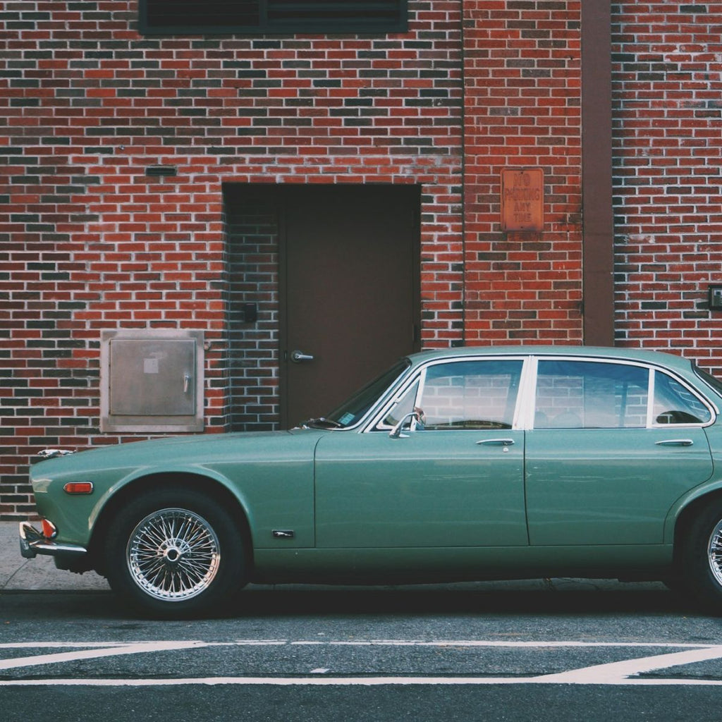 Green vintage car parked in front of a brick building