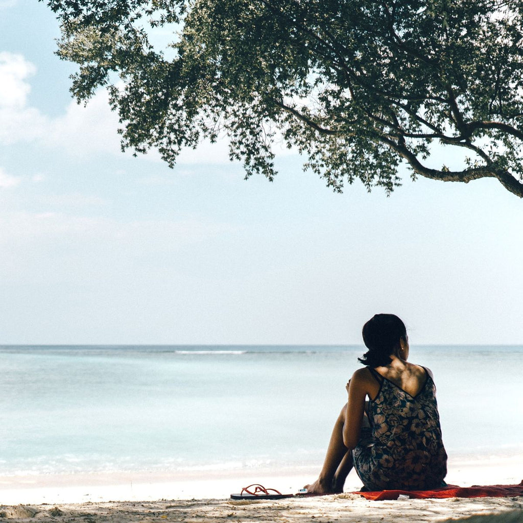 Person sitting on a log by the water under a tree