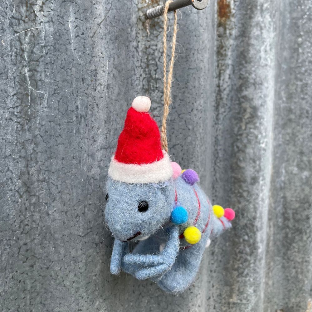 Felted dinosaur ornament in light blue with a Santa hat and Christmas lights on a textured metal surface