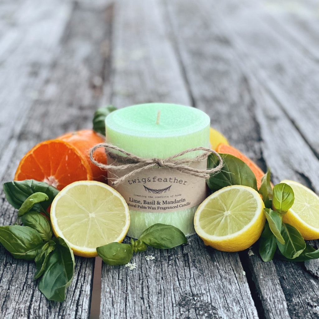 Twig and Feather Lime, Basil and Mandarin palm wax pillar candle in a lime green colour with twine packaging surrounded by citrus fruits and basil leaves on a wooden surface
