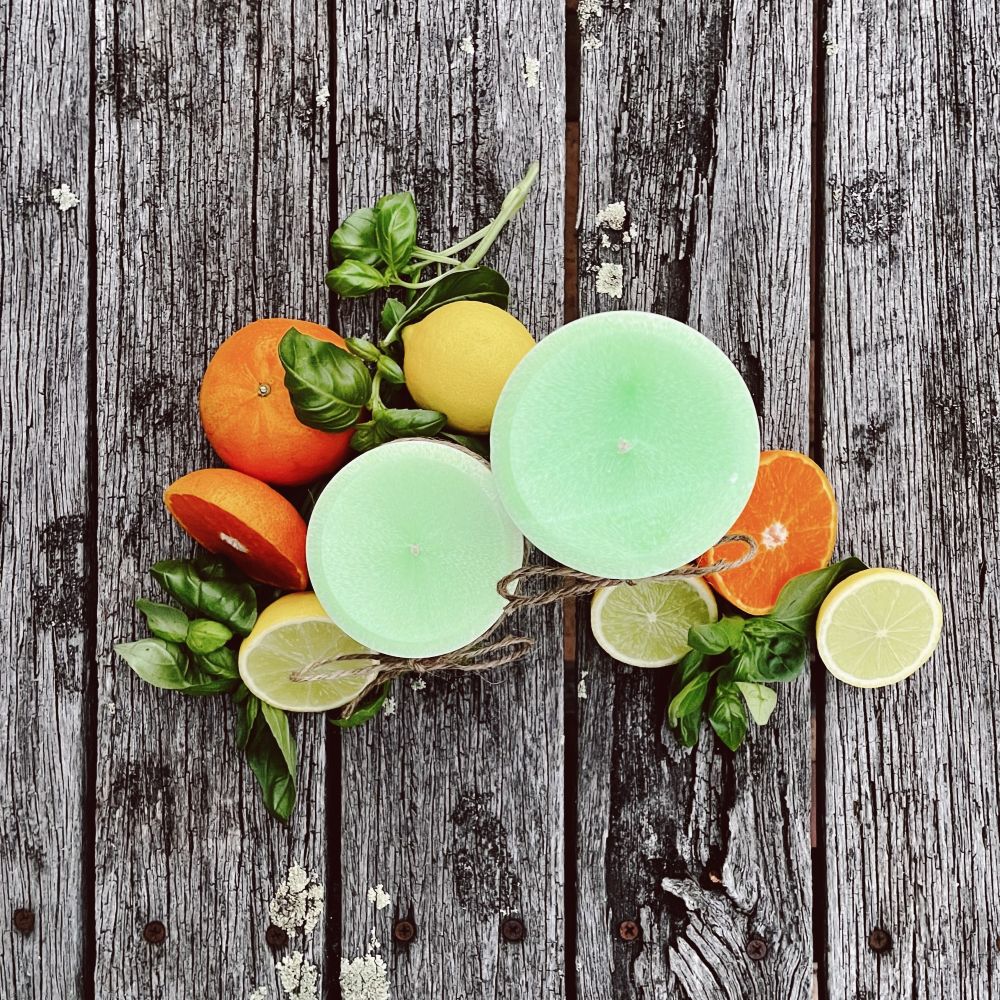 Twig and Feather Lime, Basil and Mandarin palm wax pillar candle in 2 sizes surrounded by citrus fruits and basil leaves on a wooden surface - top down view