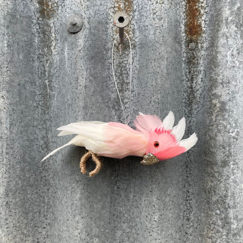 Decorative Australian Major Mitchell cockatoo decoration with glitter beak and pink and white feathers hanging on a textured metal wall.