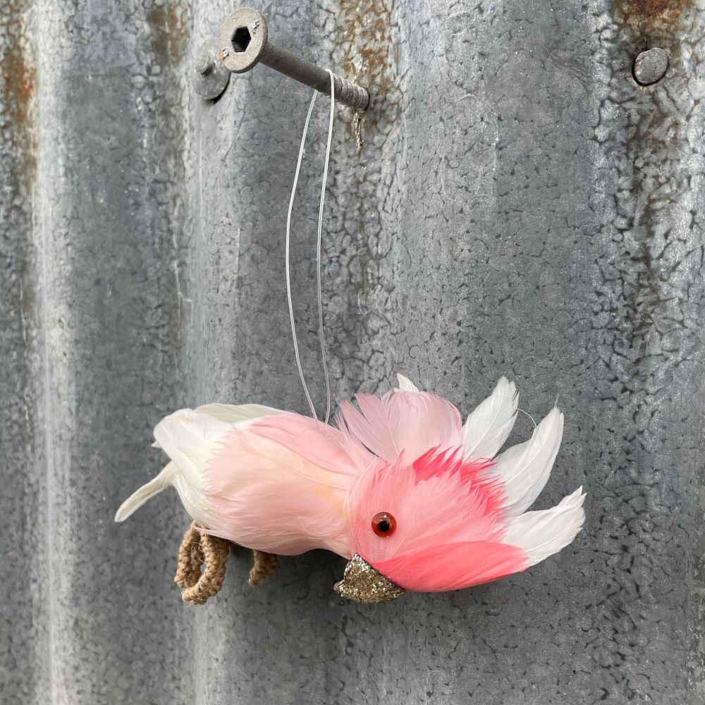 Decorative Australian Major Mitchell cockatoo decoration with glitter beak and pink and white feathers hanging on a textured metal wall - other side angle