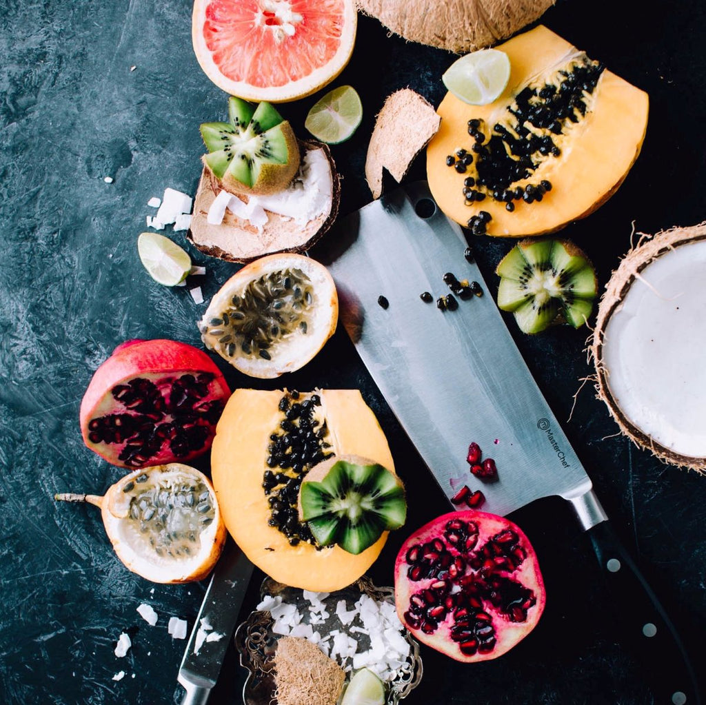 Assorted sliced fruits including papaya, passionfruit, pomegranate, and kiwi on a dark surface.