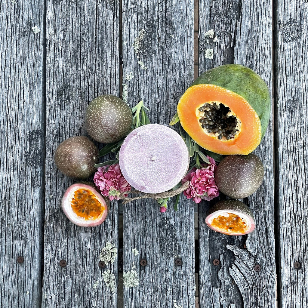 Twig and Feather Passionfruit and Papaya pillar palm wax candle surrounded by passionfruit halves, papaya, and flowers on a wooden surface - top down view